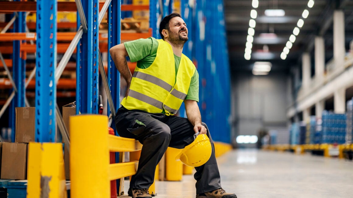 A warehouse worker having back pain and rubbing it.