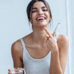 Pretty young woman brushing her teeth while looking at camera in the bathroom at home.
