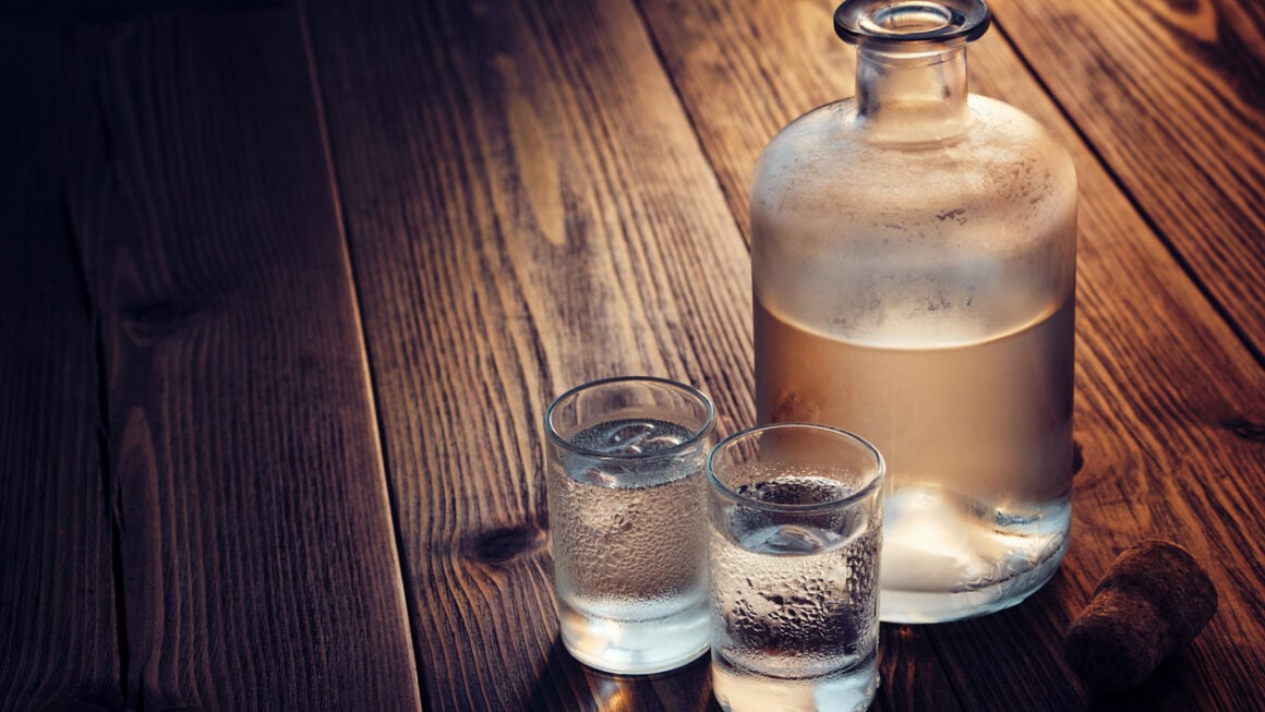 Vodka bottle and two glasses of vodka with ice on a wooden table.