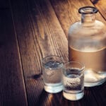 Vodka bottle and two glasses of vodka with ice on a wooden table.