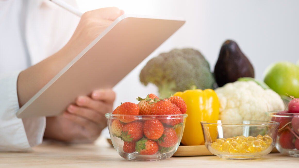 Panoramic of hand professional nutrition healthful surrounded by a variety of fresh fruits and vegetables working on digital tablet. Concept of right nutrition, diet and healthcare.