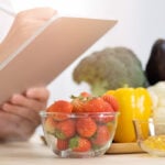 Panoramic of hand professional nutrition healthful surrounded by a variety of fresh fruits and vegetables working on digital tablet. Concept of right nutrition, diet and healthcare.