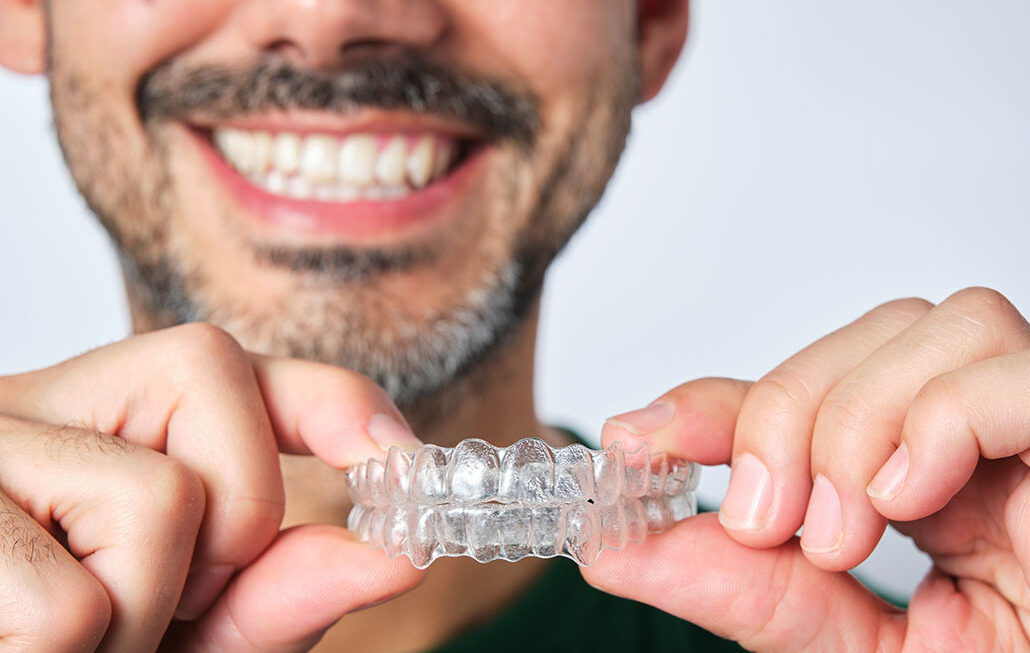 closeup man hand holding transparent retainer with unrecognizable bearded man face in unfocused background on white background