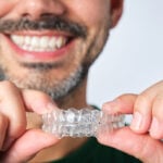 closeup man hand holding transparent retainer with unrecognizable bearded man face in unfocused background on white background