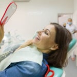 Woman patient looking in the mirror at the teeth, sitting in the dental chair.