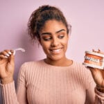Young woman smiling happy holding professional orthodontic denture with metal braces and removable invisible aligner. Comparation of two dental straighten treatments