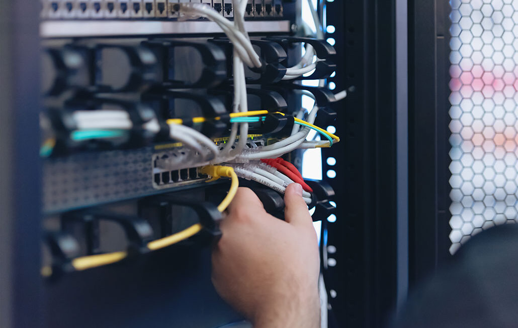 An Expert Engineer in datacenter server room connecting cables in server cabinet in network server room.
